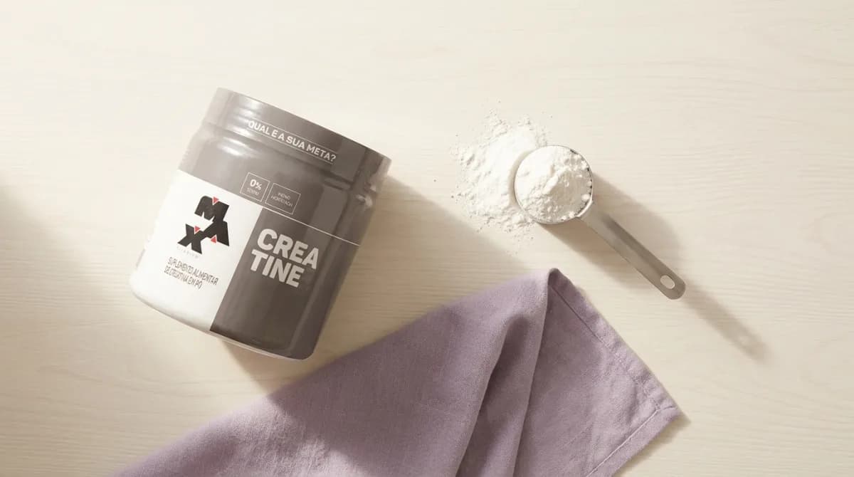 Pote de creatina Max Titanium com colher dosadora e pó branco sobre superfície clara